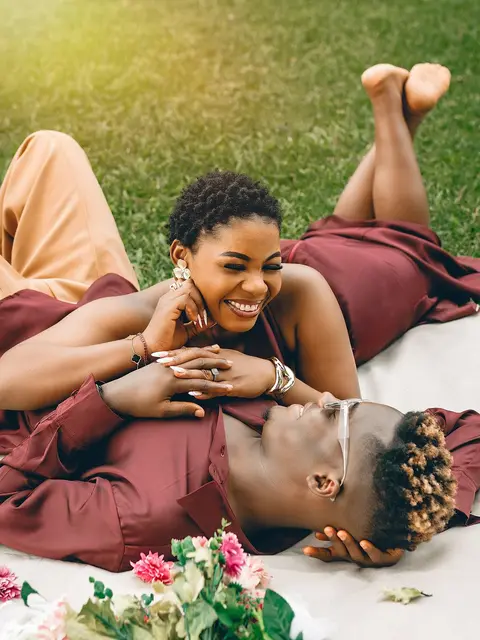 Wanandoa wamelala kwenye majani, anacheka, kichwa chake kikiwa juu yake